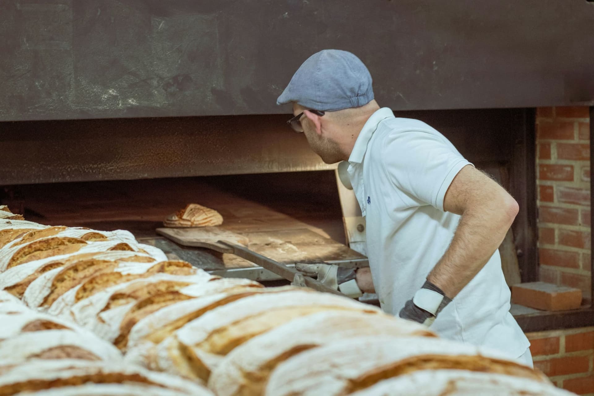 A baker lifts loaves out of a brick bread oven