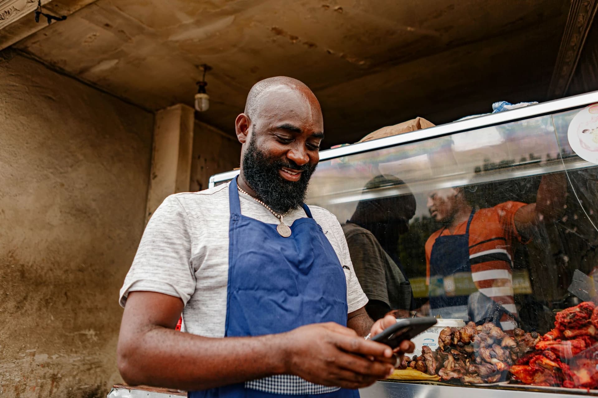 A food stall owner in an apron checks his phone